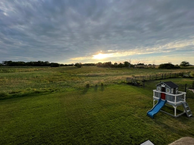 yard at dusk featuring a playground and a rural view