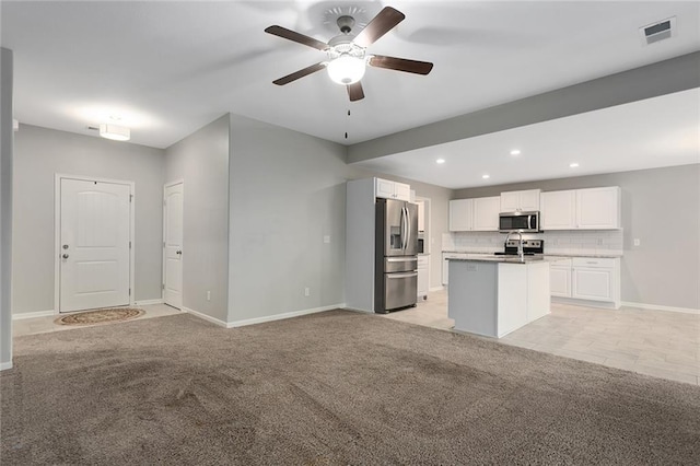 kitchen with appliances with stainless steel finishes, white cabinets, ceiling fan, a kitchen island with sink, and light colored carpet