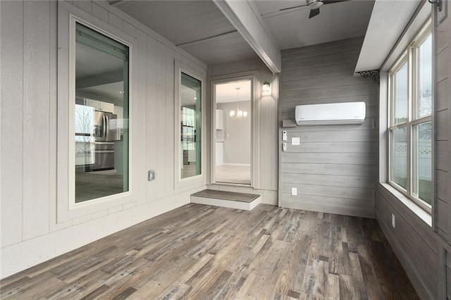 unfurnished sunroom featuring ceiling fan with notable chandelier and a wall mounted air conditioner