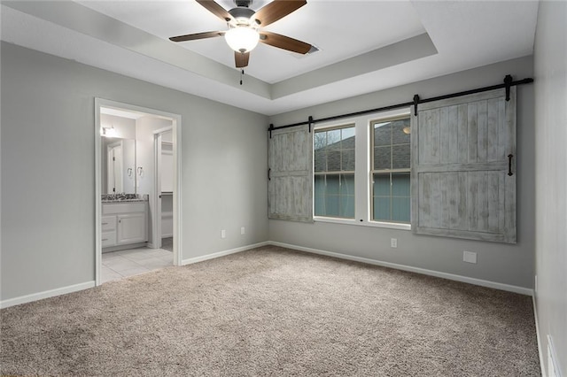 unfurnished bedroom featuring baseboards, a tray ceiling, a barn door, and light colored carpet