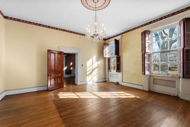 unfurnished room featuring a notable chandelier, radiator heating unit, baseboards, and wood finished floors