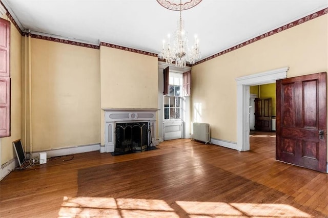 unfurnished living room featuring a fireplace with flush hearth, wood finished floors, radiator, baseboards, and a chandelier