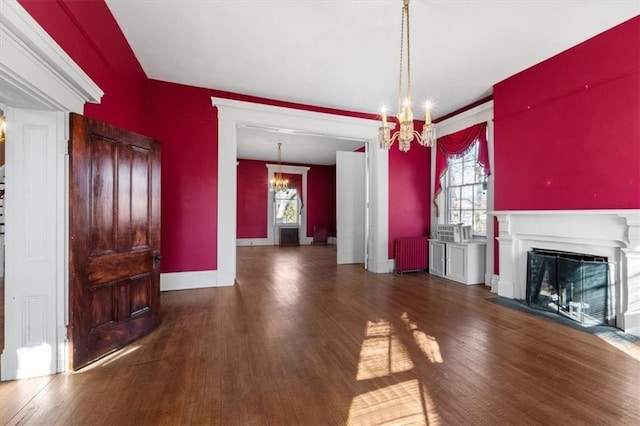 unfurnished living room with radiator, wood finished floors, baseboards, a fireplace with flush hearth, and a chandelier