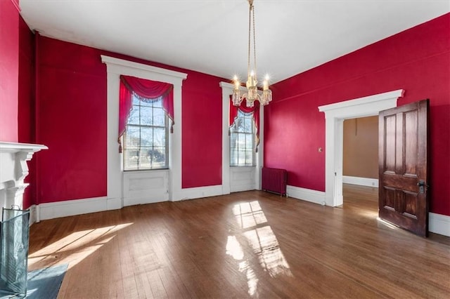 unfurnished dining area with a notable chandelier, radiator, baseboards, and wood finished floors