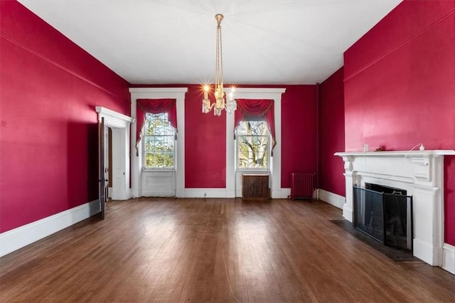 unfurnished dining area featuring baseboards, a fireplace with flush hearth, radiator heating unit, an inviting chandelier, and wood finished floors