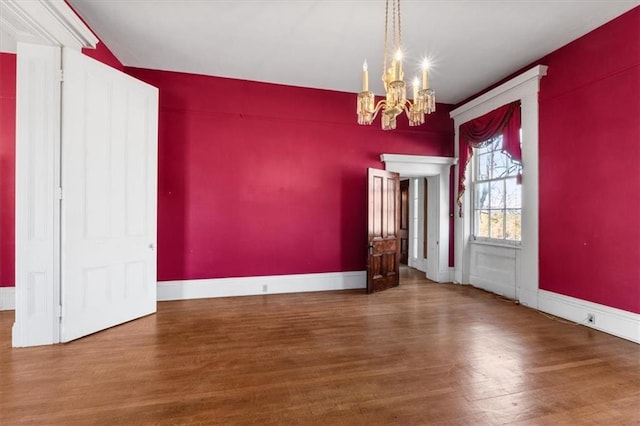 unfurnished dining area with wood finished floors, baseboards, and a chandelier