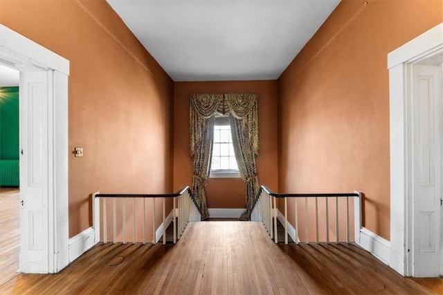 staircase with radiator, wood finished floors, and baseboards