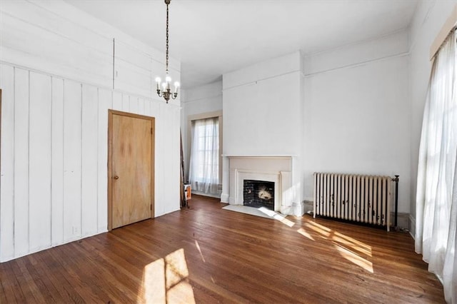 unfurnished living room with a chandelier, a fireplace with flush hearth, radiator heating unit, and wood finished floors