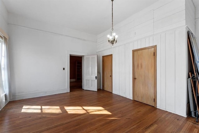 unfurnished bedroom with two closets, a notable chandelier, and wood finished floors