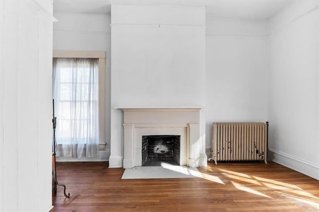 unfurnished living room featuring a fireplace with flush hearth, radiator, and wood finished floors