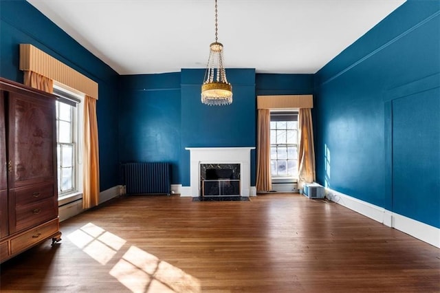 unfurnished living room featuring wood finished floors, radiator heating unit, a high end fireplace, a baseboard heating unit, and a notable chandelier