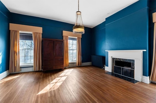 unfurnished living room with radiator, baseboards, a chandelier, a premium fireplace, and wood finished floors