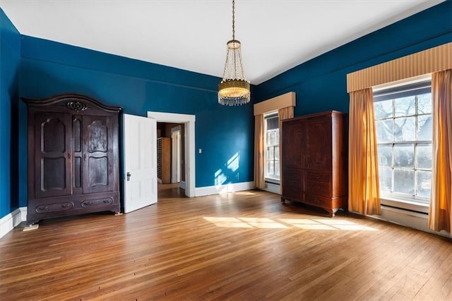 interior space with a baseboard heating unit, baseboards, a notable chandelier, and wood finished floors