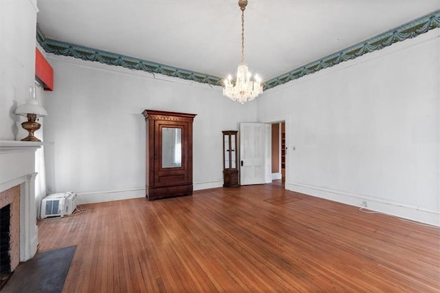 unfurnished living room featuring a wall unit AC, wood finished floors, baseboards, a fireplace with flush hearth, and a notable chandelier