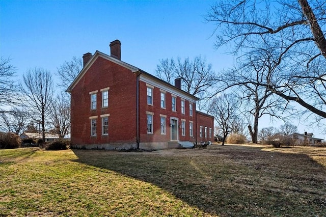 view of side of property with brick siding, a lawn, a chimney, and entry steps