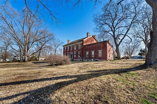 rear view of property with brick siding, a lawn, and a chimney