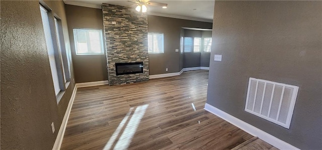 unfurnished living room with dark hardwood / wood-style flooring, a stone fireplace, ceiling fan, and crown molding