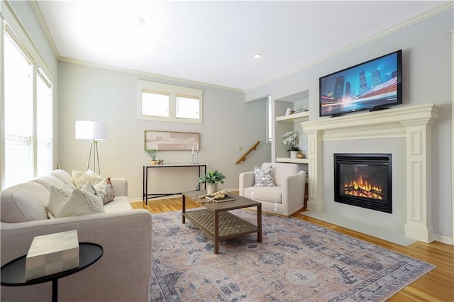 living room with a tile fireplace, built in features, a healthy amount of sunlight, and hardwood / wood-style floors