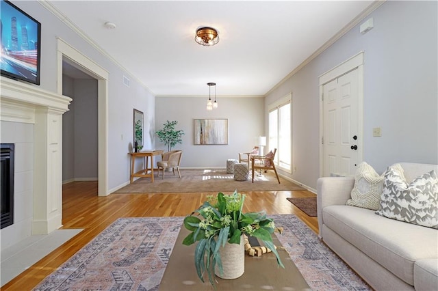 living room featuring light wood-type flooring, a tiled fireplace, and crown molding