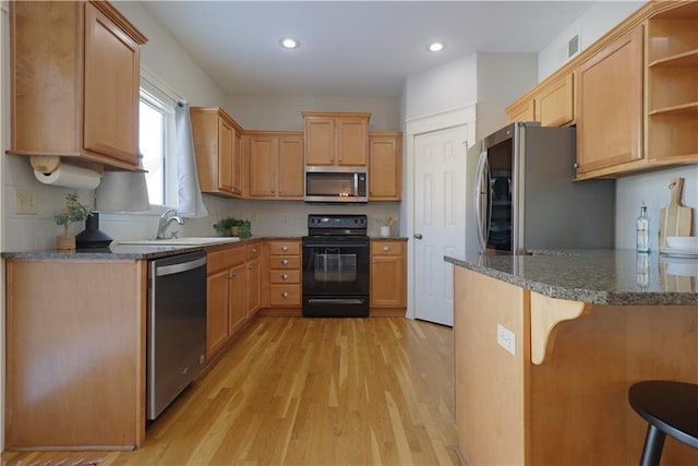 kitchen with sink, a kitchen bar, light hardwood / wood-style flooring, kitchen peninsula, and appliances with stainless steel finishes