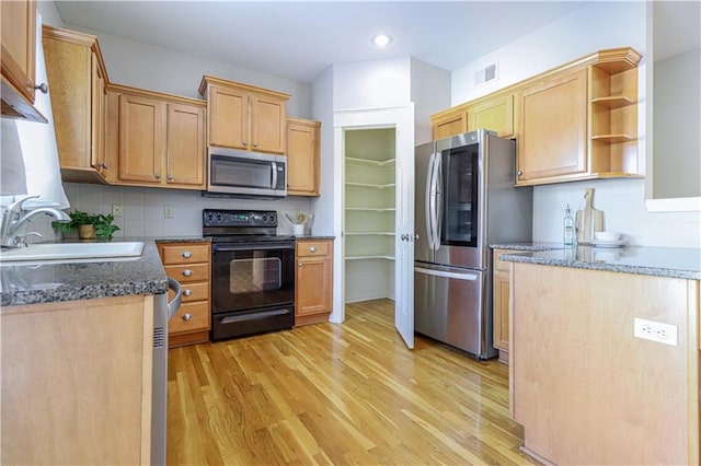 kitchen featuring sink, dark stone countertops, light wood-type flooring, backsplash, and appliances with stainless steel finishes