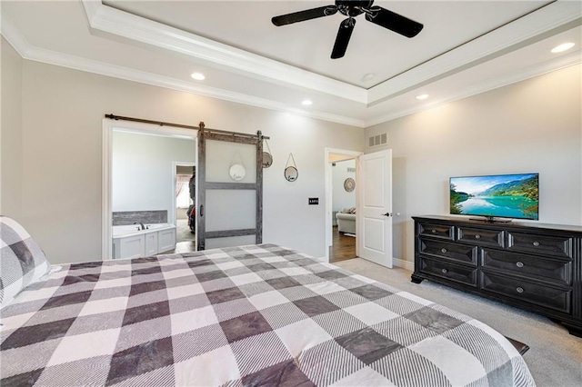 carpeted bedroom featuring ensuite bathroom, ornamental molding, a tray ceiling, ceiling fan, and a barn door