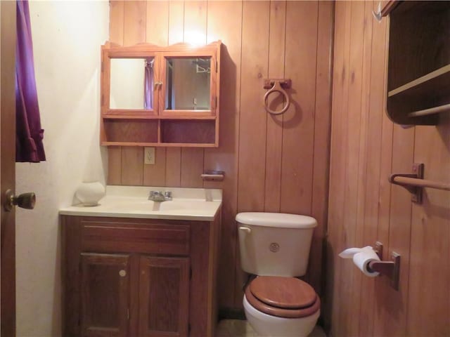 bathroom featuring vanity, toilet, and wooden walls