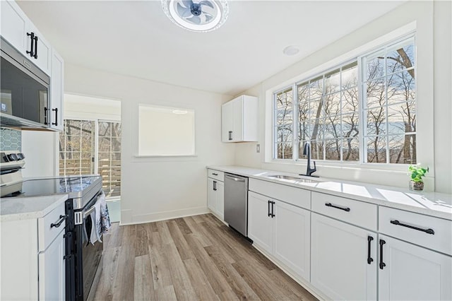 kitchen featuring sink, appliances with stainless steel finishes, white cabinetry, light stone countertops, and light wood-type flooring