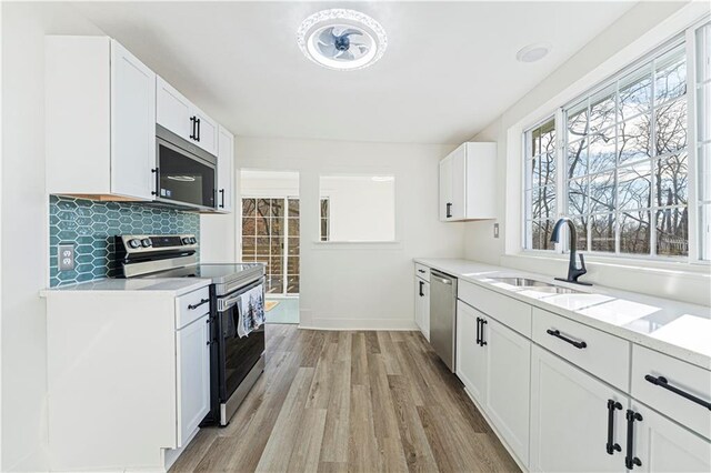 kitchen featuring white cabinetry, sink, decorative backsplash, stainless steel appliances, and light hardwood / wood-style flooring