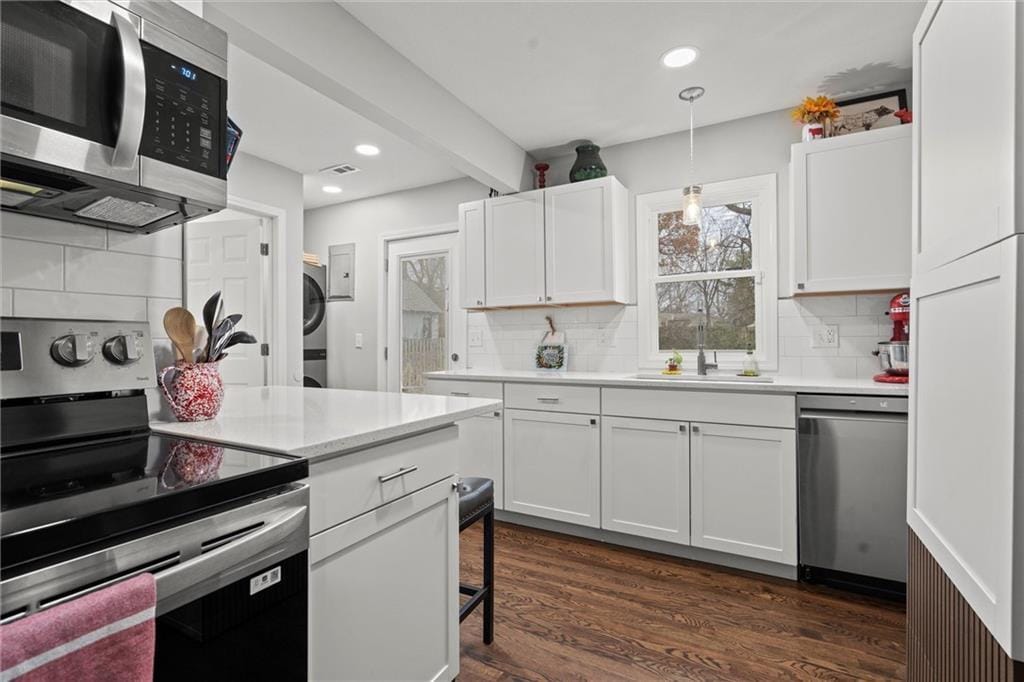 kitchen with decorative backsplash, appliances with stainless steel finishes, decorative light fixtures, stacked washer and clothes dryer, and white cabinetry