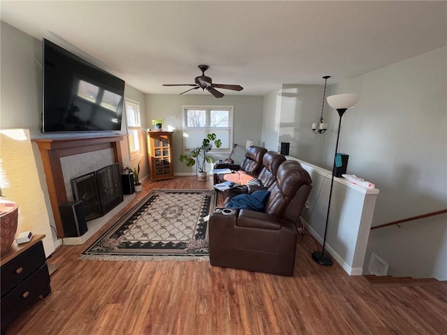 living room with wood-type flooring, a tile fireplace, and ceiling fan