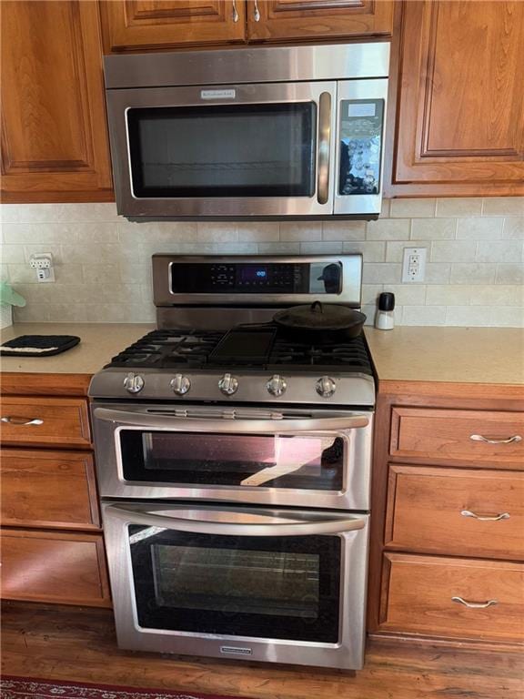 kitchen with appliances with stainless steel finishes, dark hardwood / wood-style flooring, and decorative backsplash