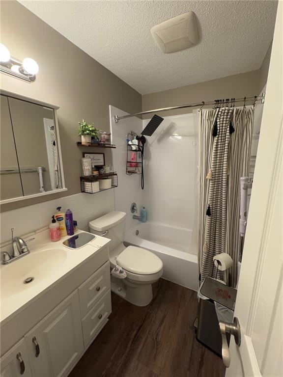 full bathroom featuring toilet, shower / tub combo, a textured ceiling, vanity, and hardwood / wood-style flooring