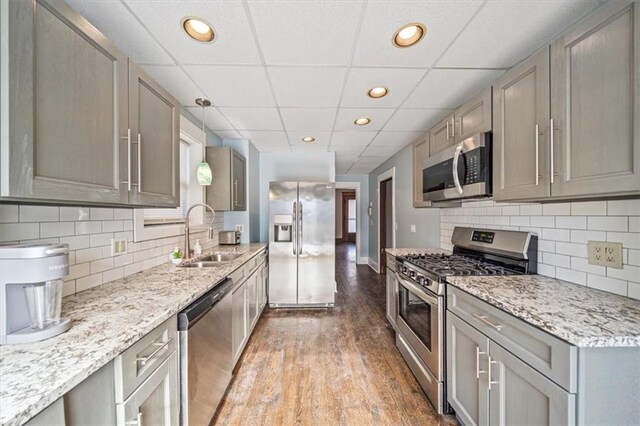 kitchen with pendant lighting, appliances with stainless steel finishes, a paneled ceiling, sink, and gray cabinetry