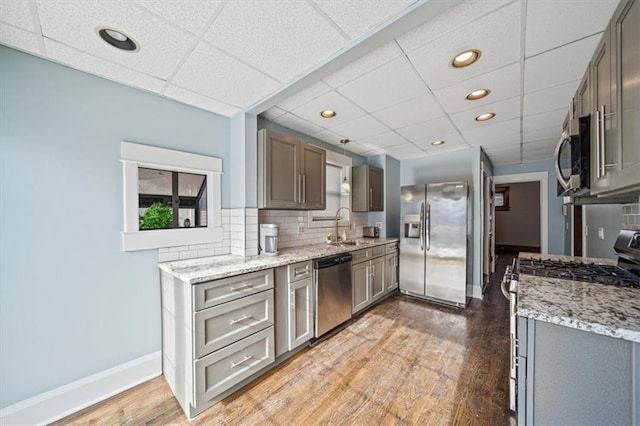 kitchen with tasteful backsplash, wood-type flooring, a drop ceiling, sink, and stainless steel appliances