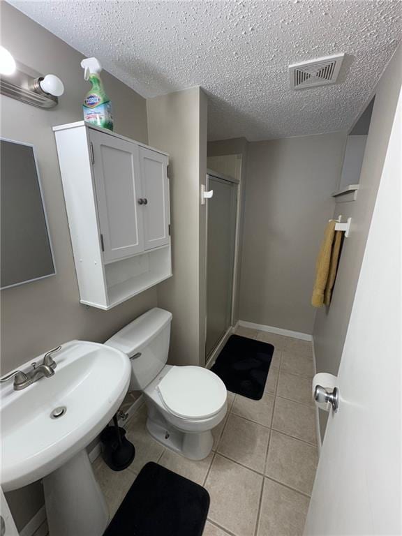 bathroom with toilet, tile patterned floors, a textured ceiling, and a shower with shower door