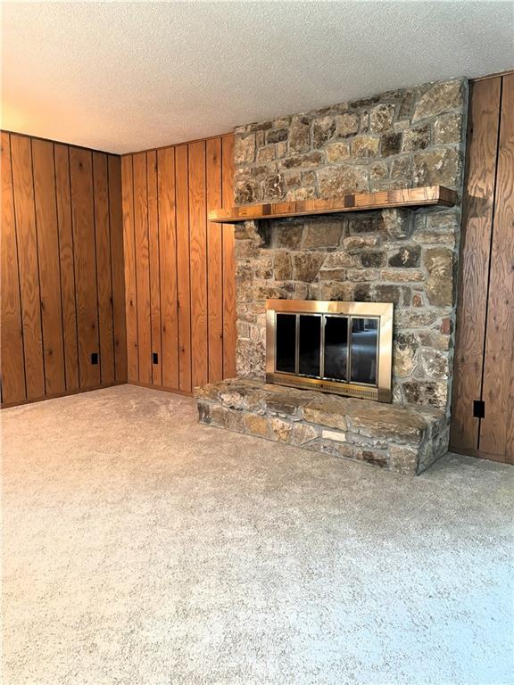 unfurnished living room featuring carpet, a textured ceiling, a stone fireplace, and wood walls