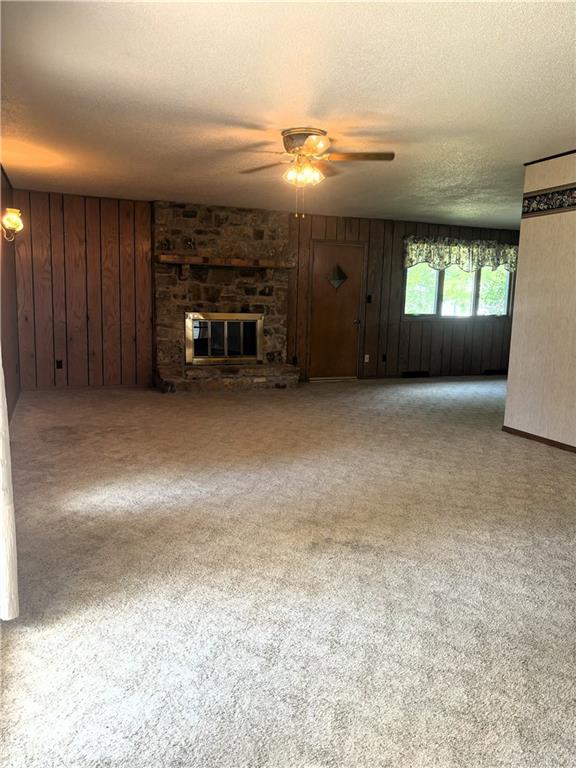 unfurnished living room with wood walls, ceiling fan, a textured ceiling, a fireplace, and light colored carpet