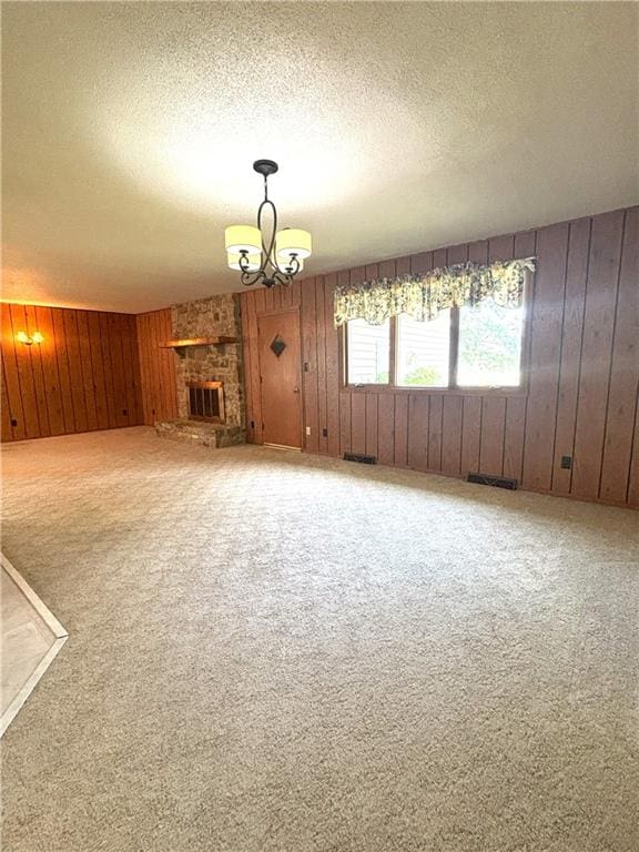 unfurnished living room featuring an inviting chandelier, a textured ceiling, wooden walls, a fireplace, and carpet