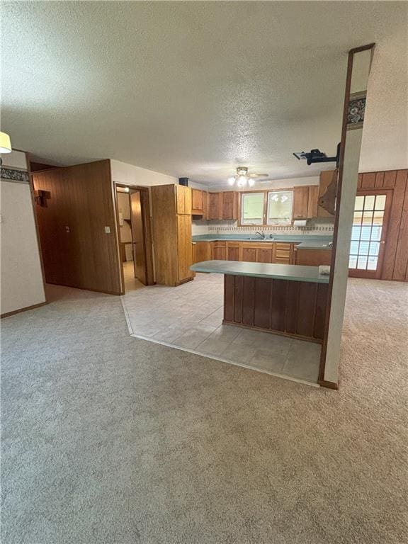 kitchen with ceiling fan, sink, kitchen peninsula, a textured ceiling, and light carpet