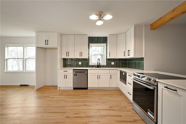 kitchen featuring stainless steel appliances, sink, light hardwood / wood-style flooring, beamed ceiling, and white cabinets