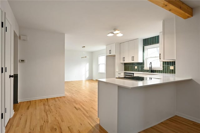 kitchen with white cabinets, light wood-type flooring, kitchen peninsula, and beamed ceiling