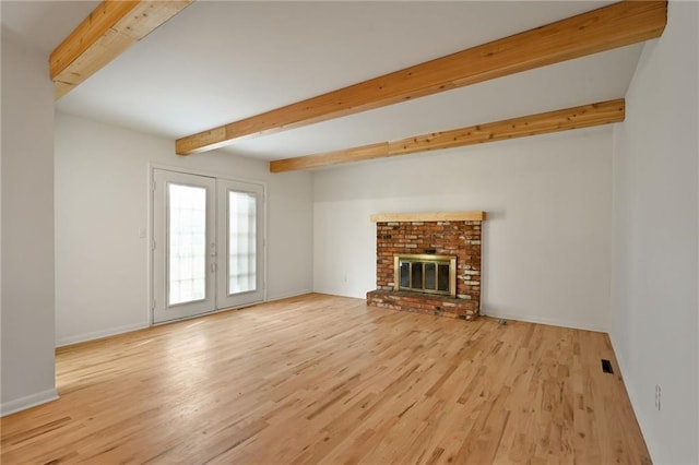 unfurnished living room with a brick fireplace, light hardwood / wood-style floors, beamed ceiling, and french doors