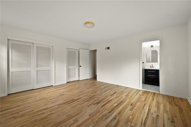 unfurnished bedroom featuring sink, two closets, ensuite bath, and light hardwood / wood-style flooring