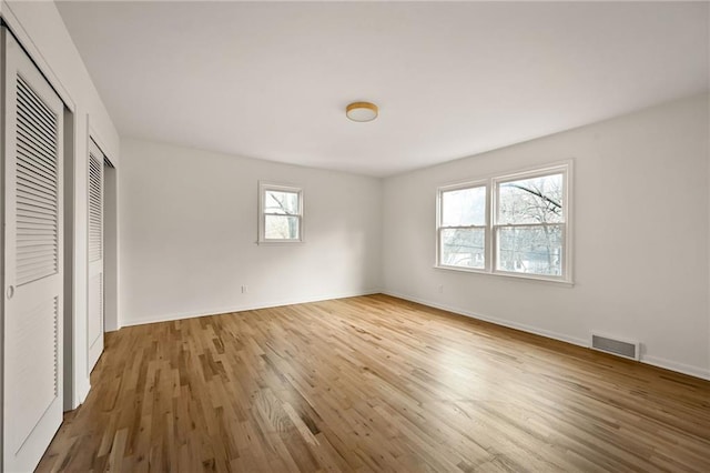 unfurnished bedroom featuring hardwood / wood-style floors, multiple windows, and two closets