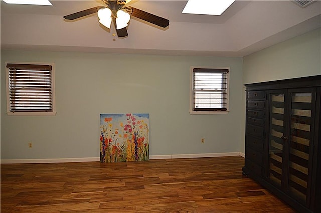 spare room with a tray ceiling, dark wood-type flooring, a skylight, and ceiling fan