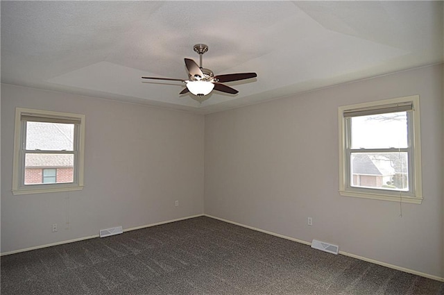 spare room featuring ceiling fan, a healthy amount of sunlight, a tray ceiling, and dark colored carpet