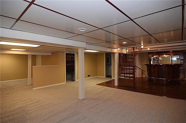 basement featuring a paneled ceiling, stacked washer / drying machine, and carpet floors