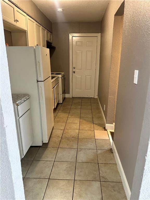 kitchen with light stone countertops, light tile patterned floors, white cabinets, and white appliances