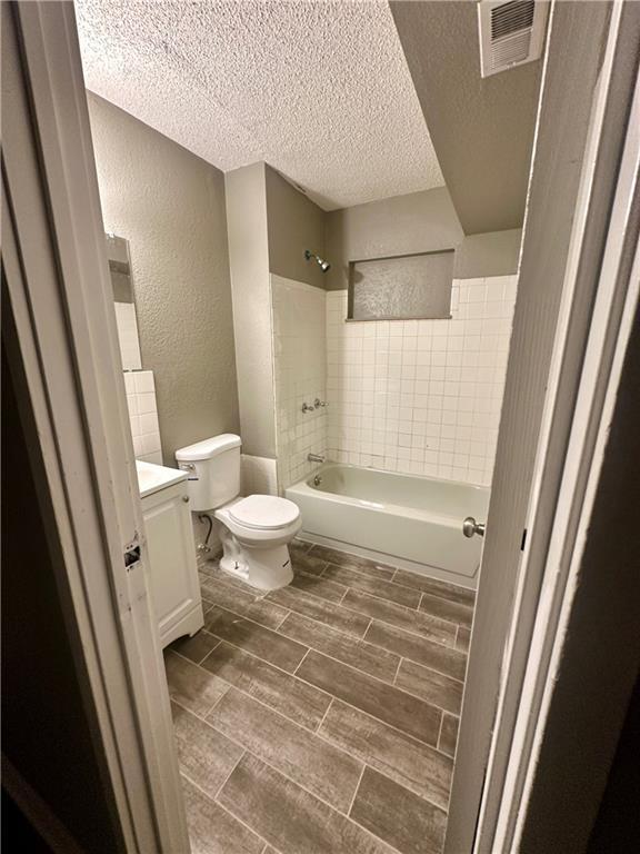 full bathroom with a textured ceiling, vanity, tiled shower / bath combo, and toilet